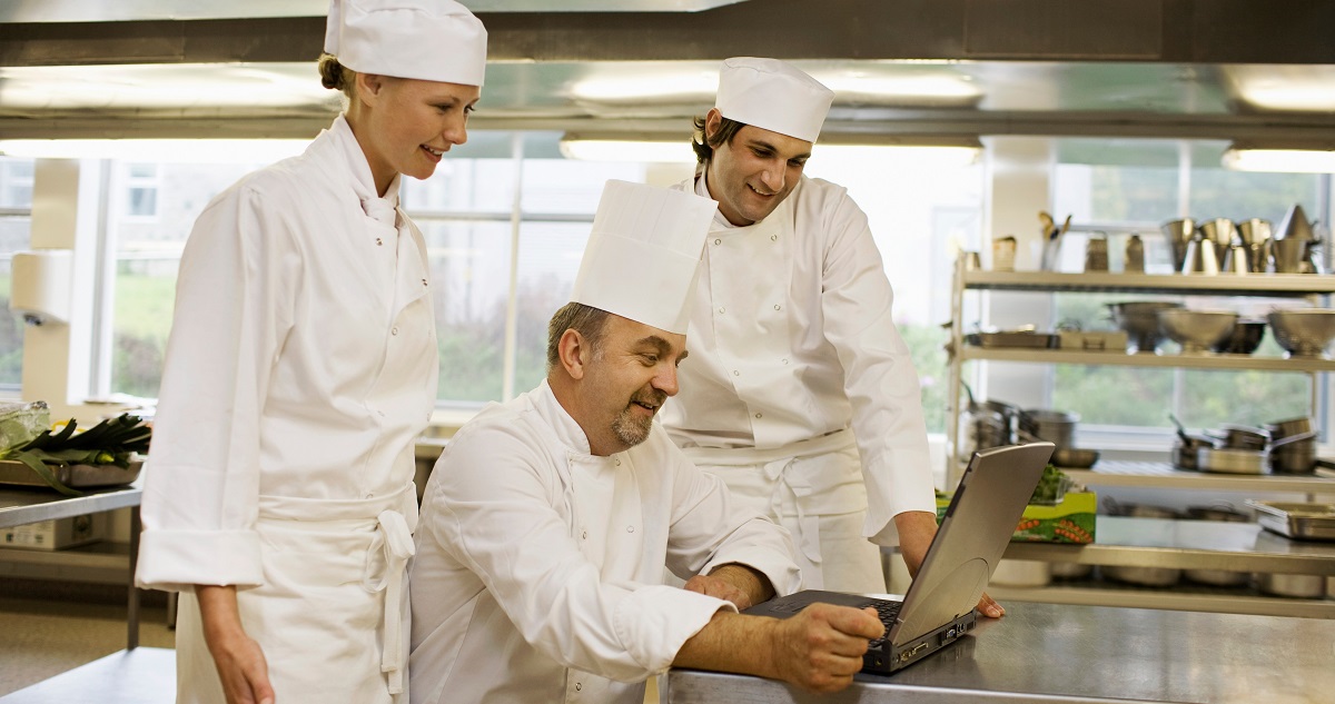 Three chefs looking at a laptop
